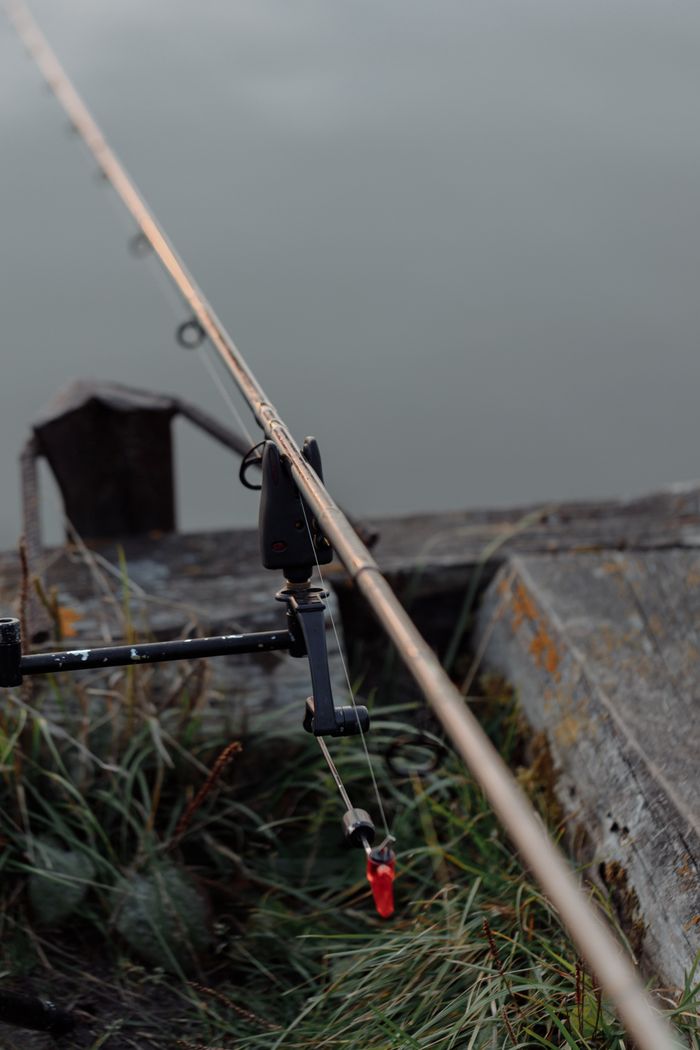 Close-up of a fishing rod and equipment on a riverbank, showcasing a peaceful outdoor fishing scene.