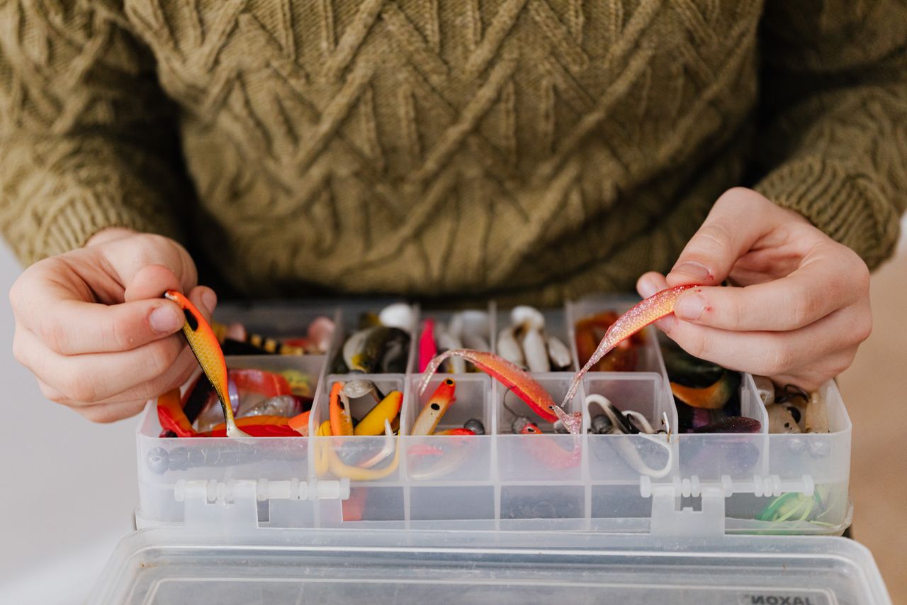 Close-up of hands organizing colorful fishing lures in a tackle box, perfect for anglers.