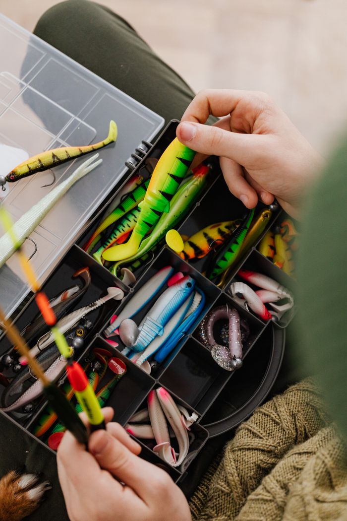 Bright fishing lures and equipment in an organized tackle box being handled.
